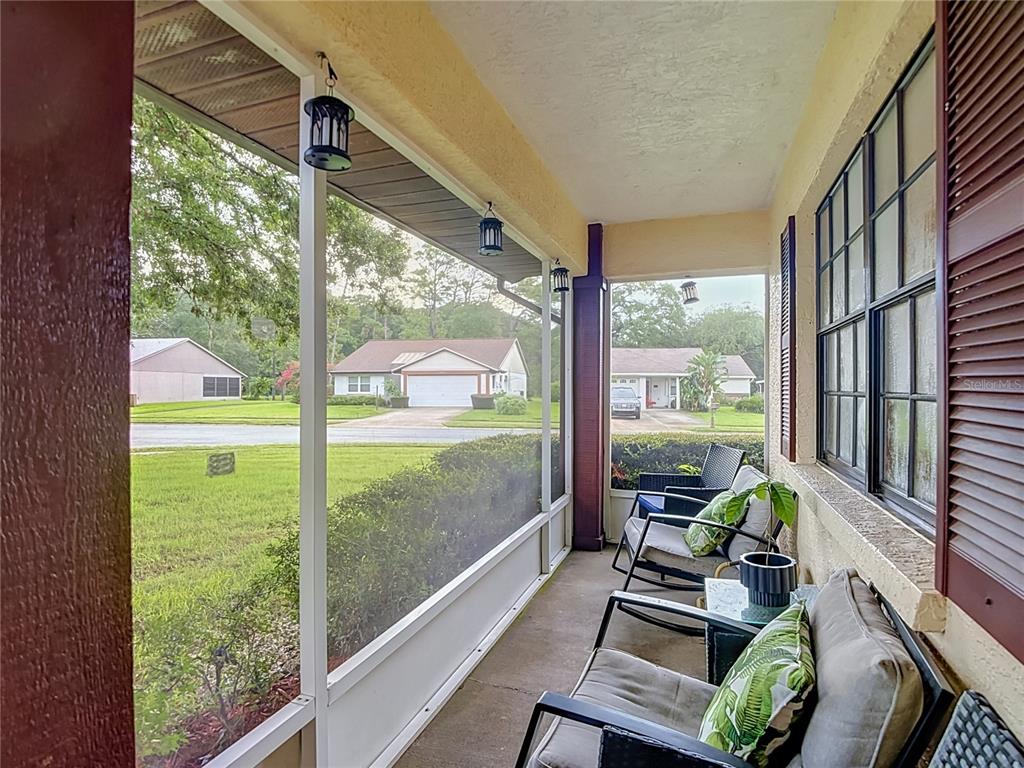 A screened-in porch features outdoor seating, a concrete floor, and views of a suburban street — 7407 BALTUSROL DRIVE, NEW PORT RICHEY, FL