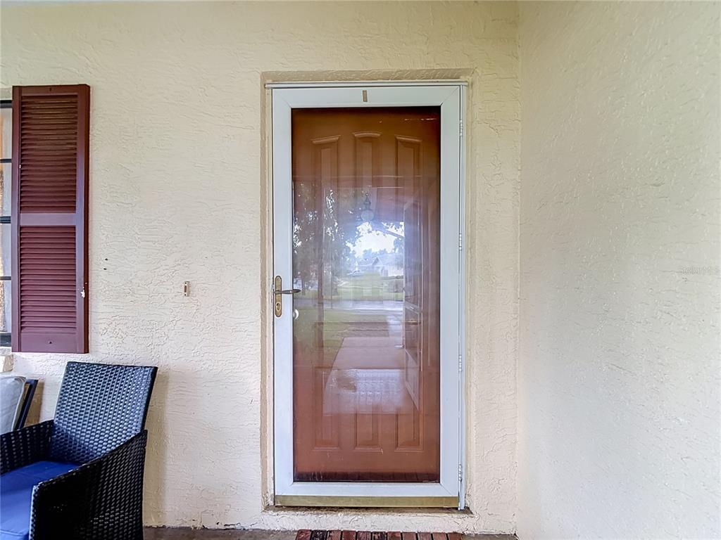 A white storm door with a brown interior door is set into a beige stucco wall — 7407 BALTUSROL DRIVE, NEW PORT RICHEY, FL