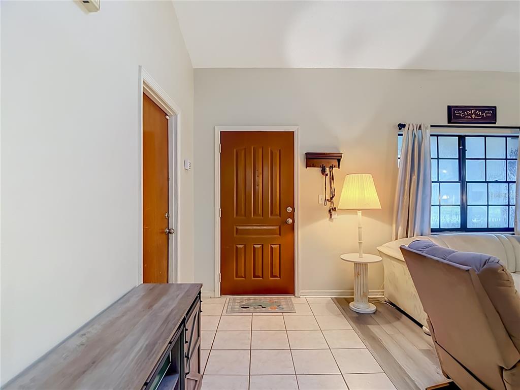 An entryway features a brown front door, tiled flooring, a lamp on a pedestal table, and a closet — 7407 BALTUSROL DRIVE, NEW PORT RICHEY, FL