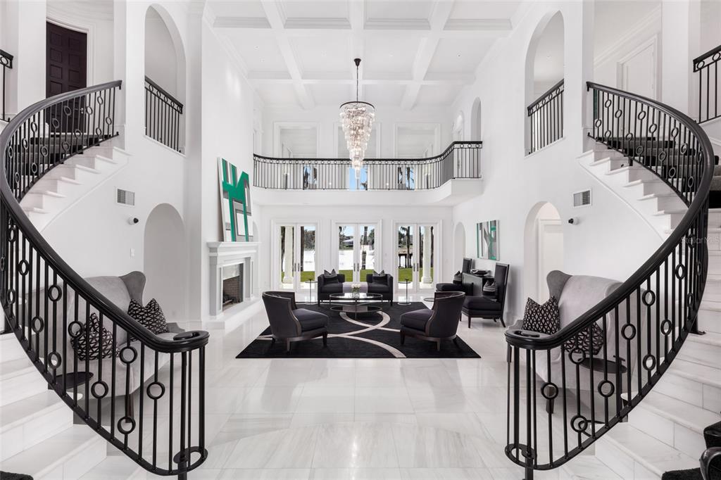A grand foyer features dual curved staircases, a coffered ceiling, and a central seating area — 12488 PARK AVENUE, WINDERMERE, FL