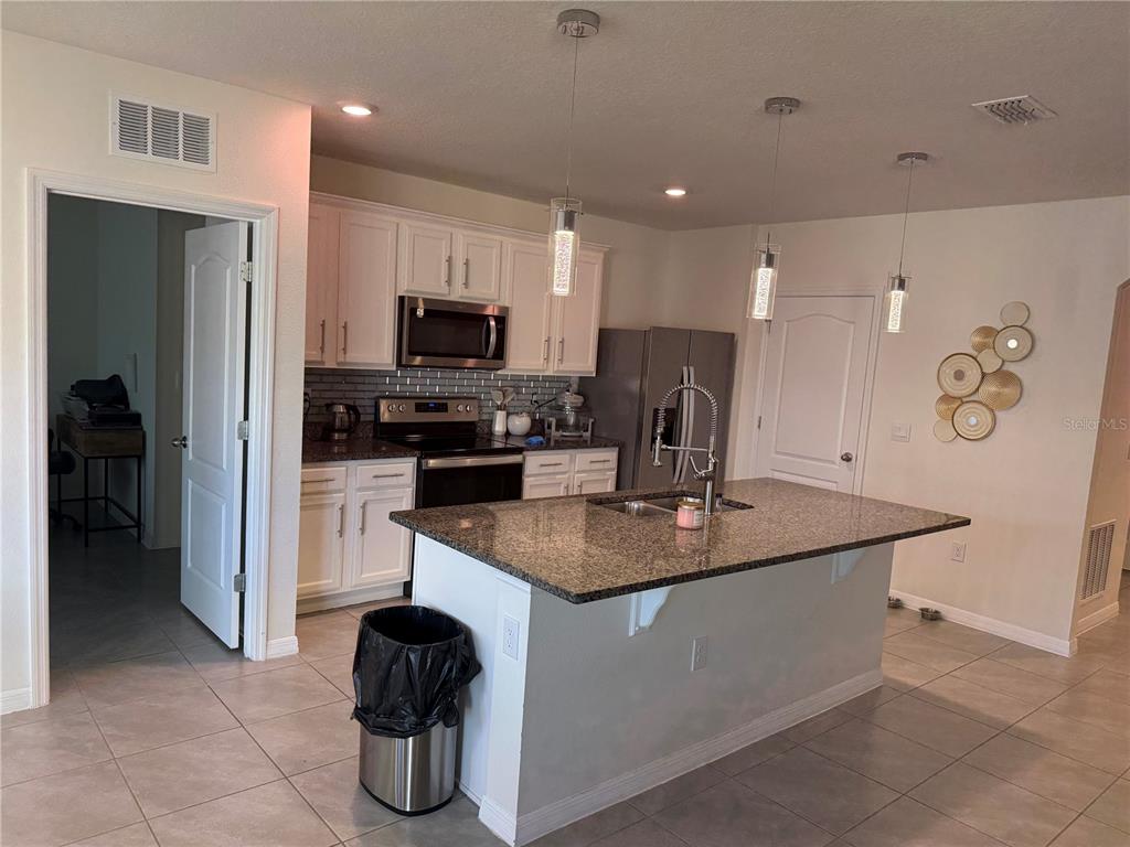 A kitchen features white cabinets, granite countertops, a center island, and stainless steel appliances — 2541 HARMONIA HAMMOCK ROAD, ST CLOUD, FL