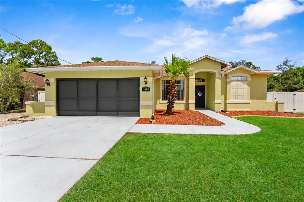 A single-story house with a yellow stucco exterior, a dark garage door, and a palm tree — 11303 TOPAZ STREET, SPRING HILL, FL