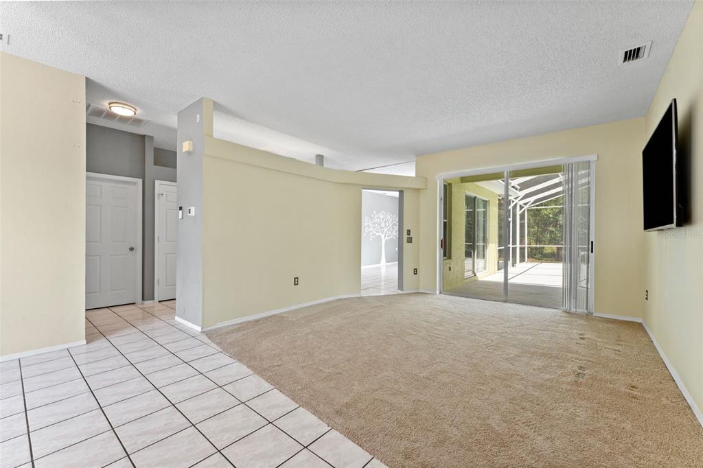 A living room with beige carpet, tile flooring, a sliding glass door, and yellow walls — 11303 TOPAZ STREET, SPRING HILL, FL