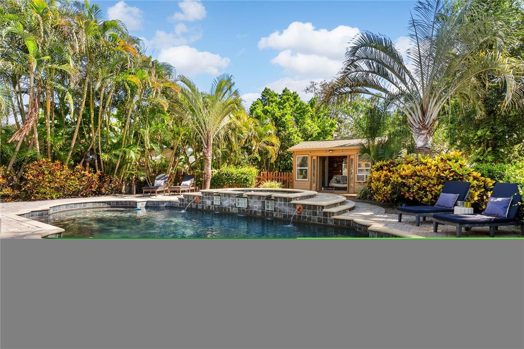 A swimming pool with a stone fountain feature sits in a backyard with palm trees — 20 BOGIE LANE, PALM HARBOR, FL