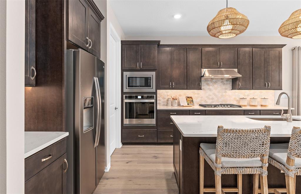 A kitchen features dark wood cabinetry, stainless steel appliances, a white island, and woven pendant lights — 5094 SUNFALLS AVENUE, ST CLOUD, FL