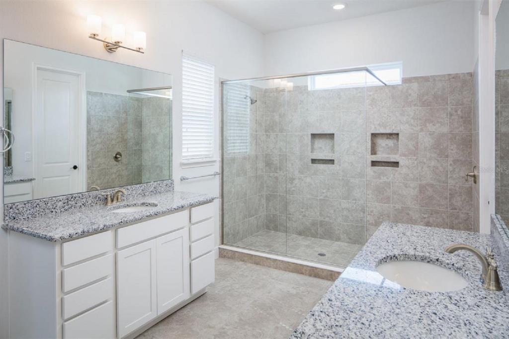 A bathroom features dual granite vanities, white cabinetry, and a large glass-enclosed tiled walk-in shower — 6677 WAKE STREET, ST CLOUD, FL