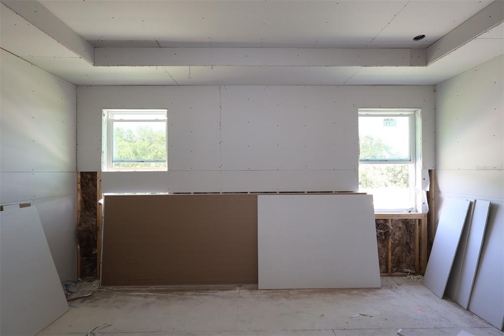 An unfinished room with exposed insulation, drywall panels, and two windows under construction — 2879 SWEETGRASS LANE, ZELLWOOD, FL