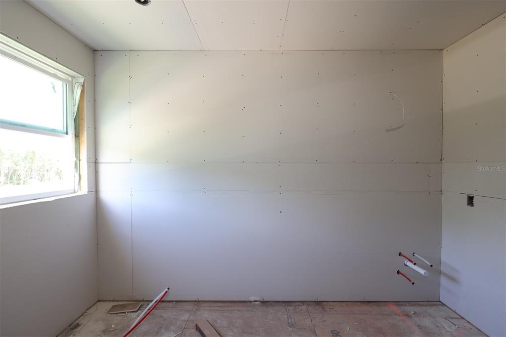 An unfinished room with bare drywall, exposed plumbing pipes, and a window on the left — 2879 SWEETGRASS LANE, ZELLWOOD, FL