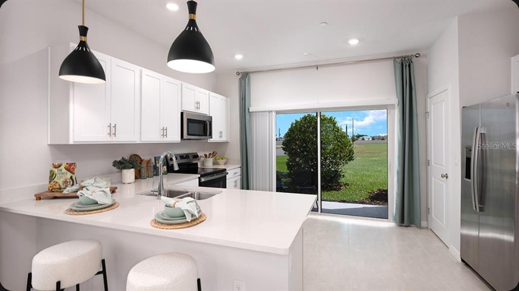 A modern kitchen features white cabinets, quartz countertops, stainless steel appliances, and a sliding glass door — 2790 ARMADALE DRIVE UNIT 2790, MOUNT DORA, FL
