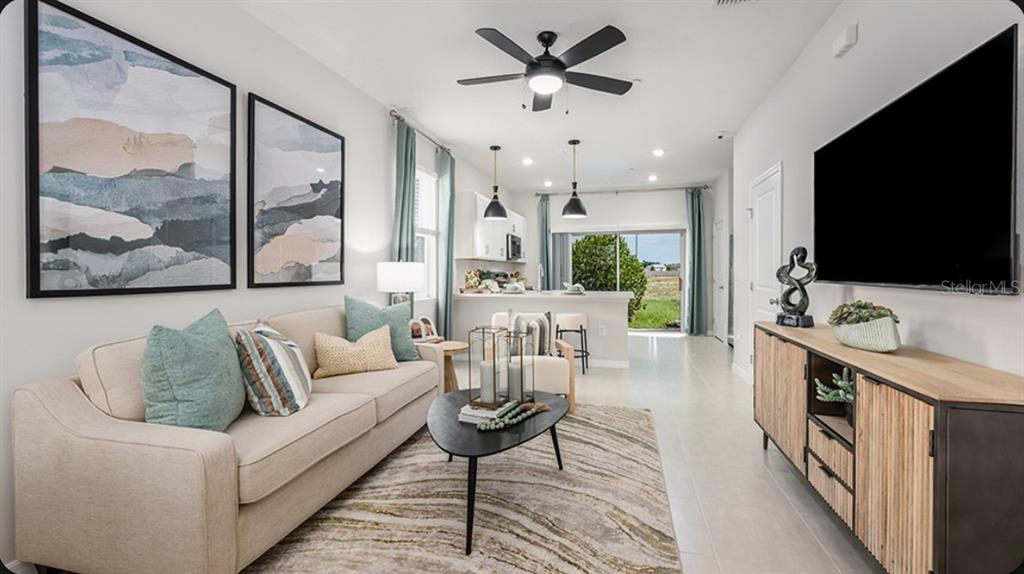 A living room features a beige sofa, a television, and an open-concept kitchen beyond — 2790 ARMADALE DRIVE UNIT 2790, MOUNT DORA, FL