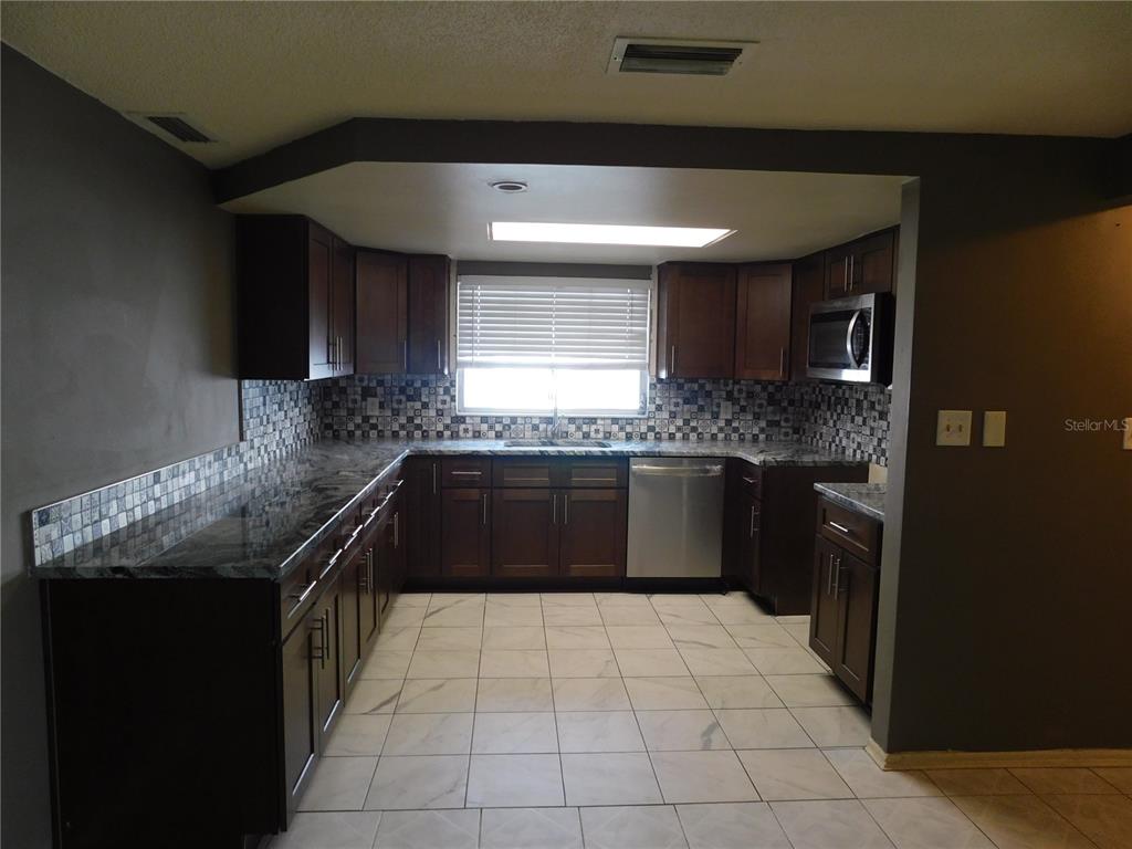 A kitchen features dark wood cabinets, granite countertops, a patterned tile backsplash, and tile flooring — 3220 COLDWELL DRIVE, HOLIDAY, FL