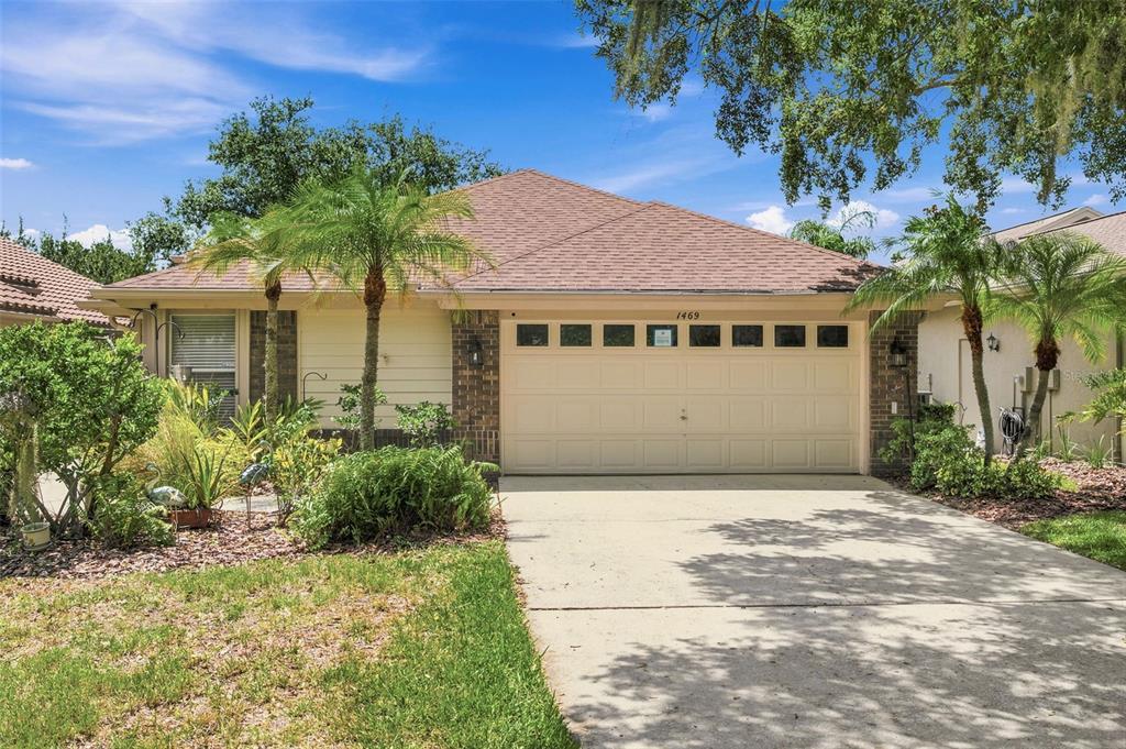 A single-story house with a beige exterior, brick accents, a two-car garage, and palm trees — 1469 RIVERDALE DRIVE, OLDSMAR, FL