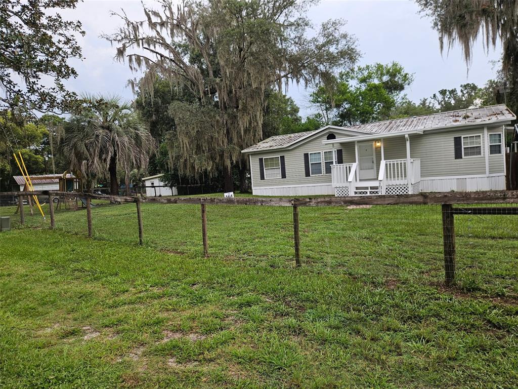A light green manufactured home sits behind a wooden fence on a grassy lot — 5815 N TSALA APOPKA DRIVE, HERNANDO, FL