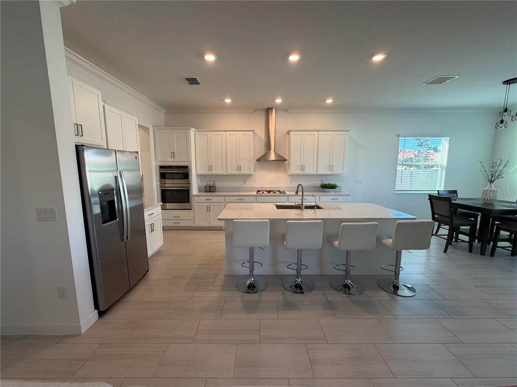 A modern kitchen features white cabinetry, stainless steel appliances, a large island, and tile flooring — 17165 SCUBA CREST STREET, WIMAUMA, FL