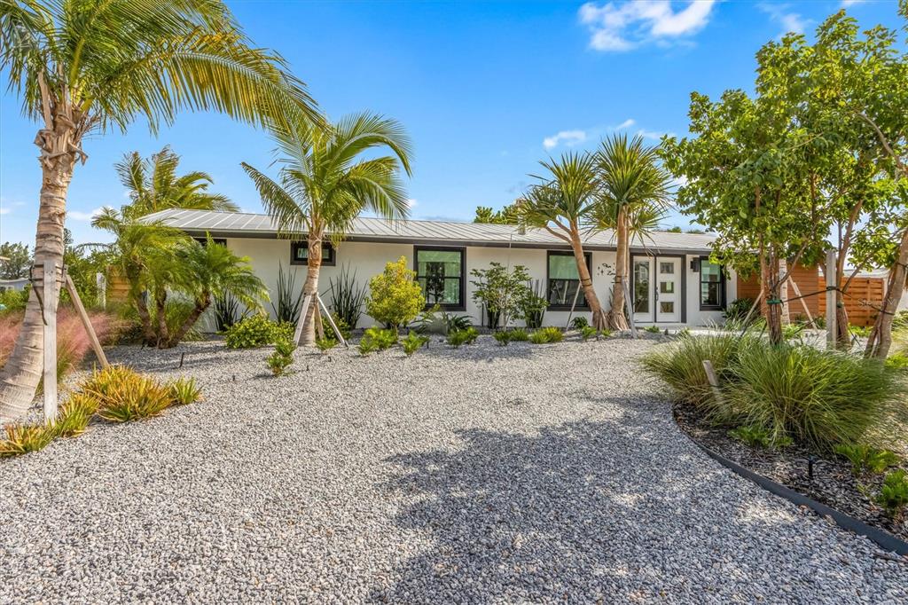 A single-story white house with a metal roof and gravel front yard under palm trees — 505 65TH STREET, HOLMES BEACH, FL