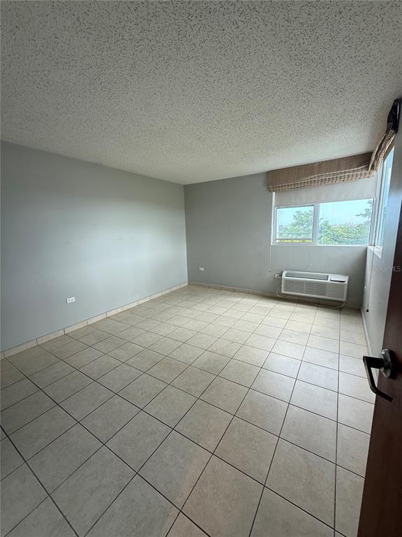 An empty room features light gray walls, tiled flooring, a popcorn ceiling, and a window unit — 155 CARRAZO UNIT 8D, GUAYNABO, PR