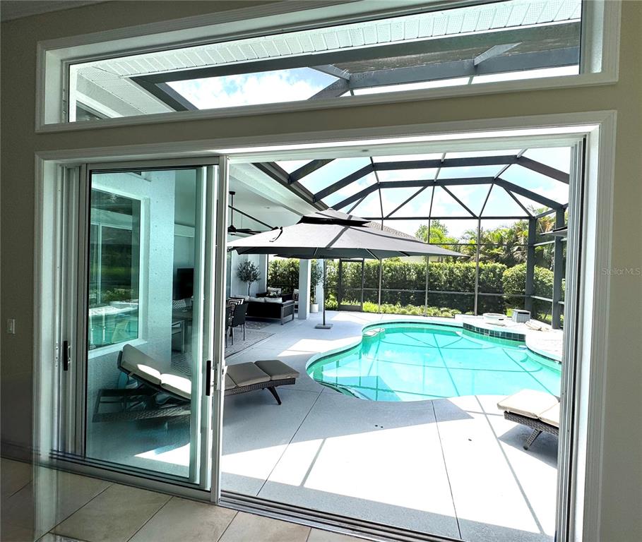A view through sliding glass doors reveals a screened-in patio with a pool and umbrella — 1539 ORMOND TERRACE, PARRISH, FL