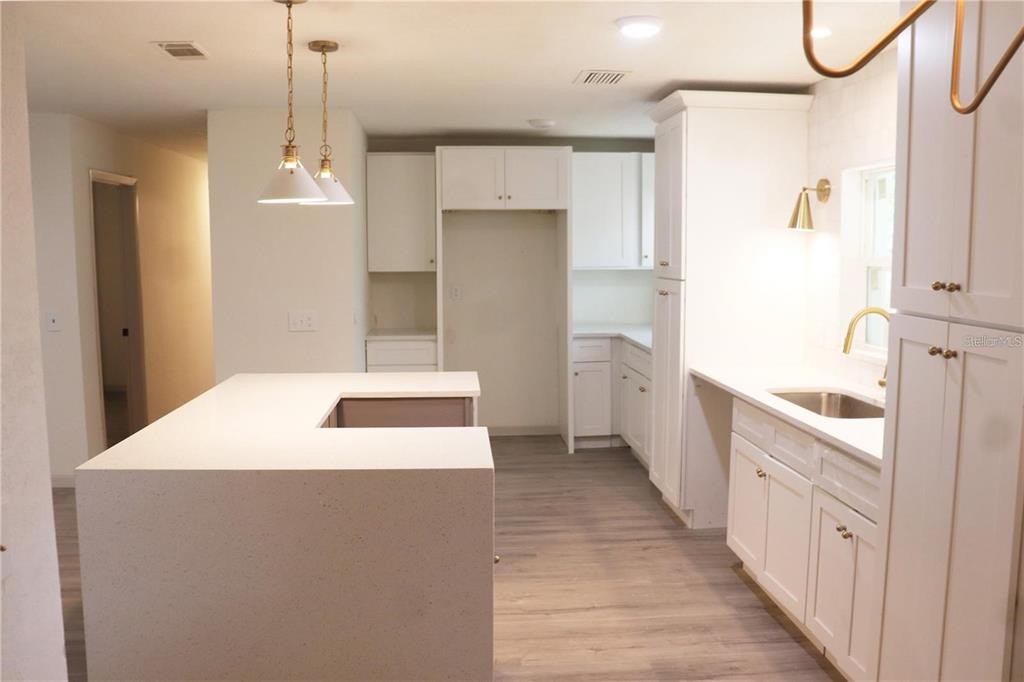 A modern kitchen features white cabinetry, a quartz island, and light wood-look flooring — 1604 STARFIRE LANE, OCOEE, FL