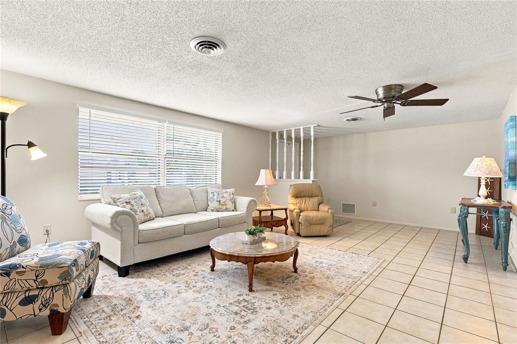 A living room features a beige sofa, patterned armchair, tile flooring, and a ceiling fan — 411 PLANTATION ROAD, VENICE, FL