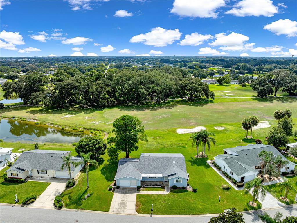 An aerial view shows three suburban houses situated along a golf course with a pond — 17873 SE 99TH AVENUE, SUMMERFIELD, FL