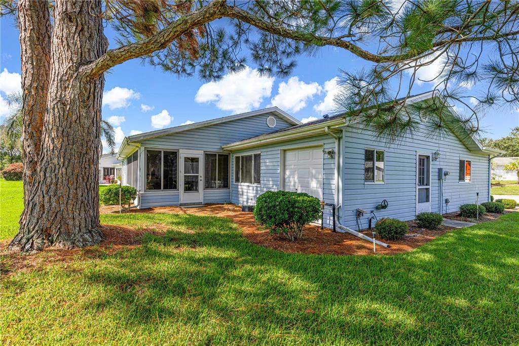 A light blue single-story house with a garage and a screened porch under a tree — 17873 SE 99TH AVENUE, SUMMERFIELD, FL