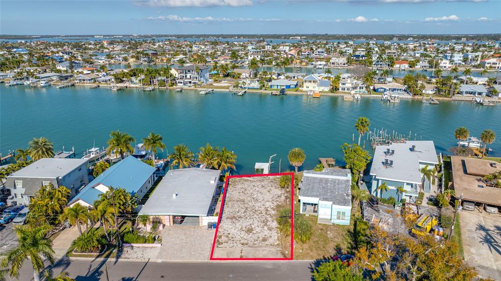 An aerial view shows a vacant waterfront lot outlined in red between two existing houses — 11075 3RD STREET E, TREASURE ISLAND, FL