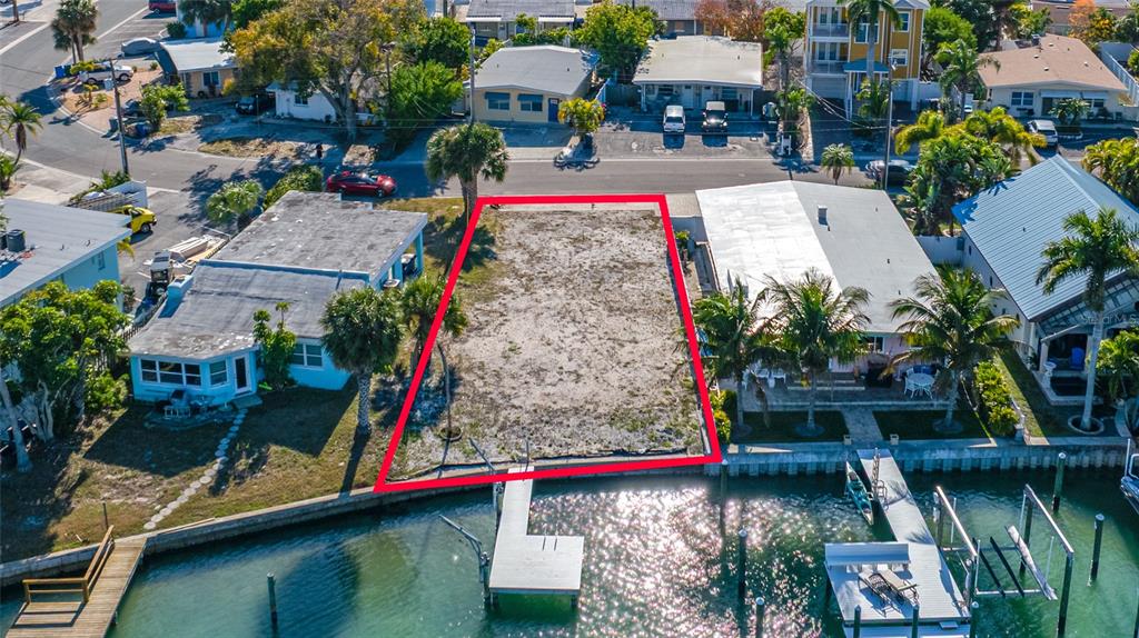 An aerial view shows a vacant waterfront lot outlined in red between two houses — 11075 3RD STREET E, TREASURE ISLAND, FL