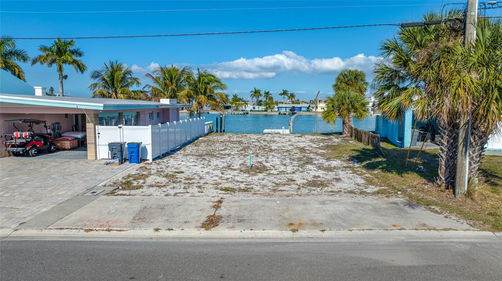 A vacant waterfront lot sits between two houses with a concrete driveway and palm trees — 11075 3RD STREET E, TREASURE ISLAND, FL