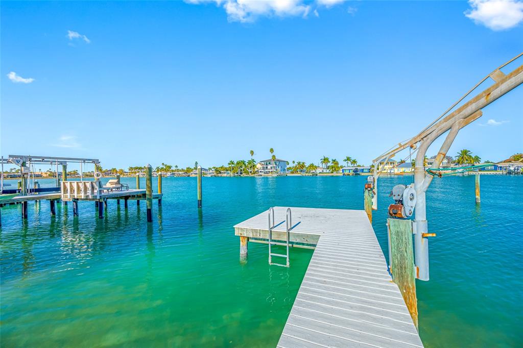 A wooden dock extends into a turquoise canal with a boat lift and pilings — 11075 3RD STREET E, TREASURE ISLAND, FL
