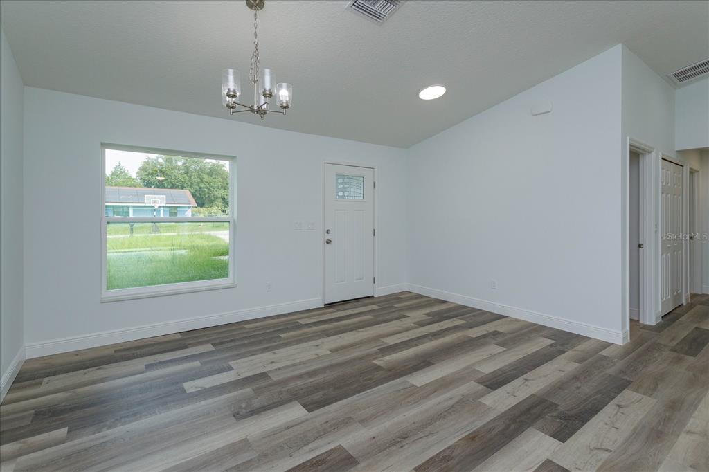 An empty room features white walls, wood-look flooring, a chandelier, and a front entry door — 31 PINE RUN TERRACE, OCALA, FL
