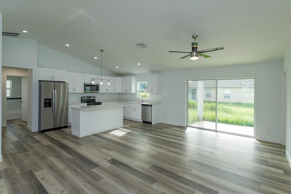 An open-concept kitchen and living area with white cabinets, stainless appliances, and wood-look flooring — 31 PINE RUN TERRACE, OCALA, FL