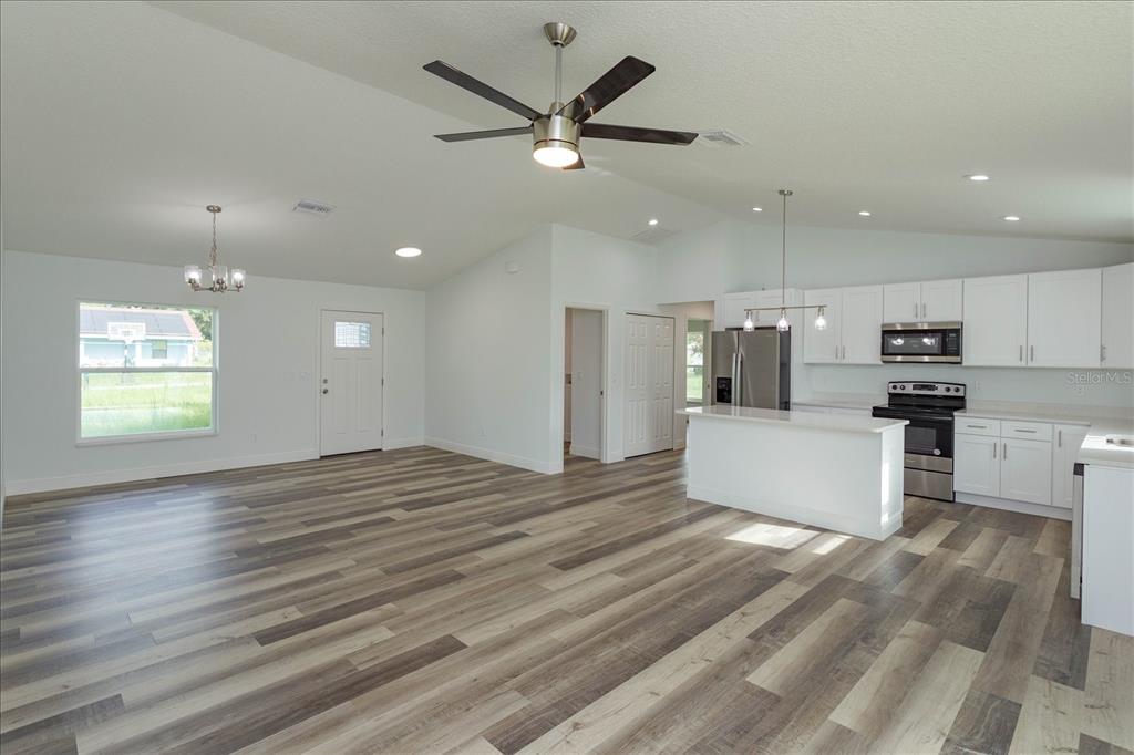 An open-concept kitchen and living area featuring white cabinets, stainless steel appliances, and wood-look flooring — 31 PINE RUN TERRACE, OCALA, FL