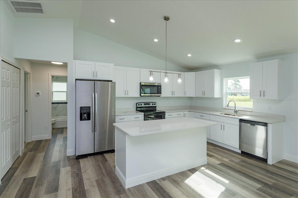 A modern kitchen features white cabinets, stainless steel appliances, a center island, and wood-look flooring — 31 PINE RUN TERRACE, OCALA, FL