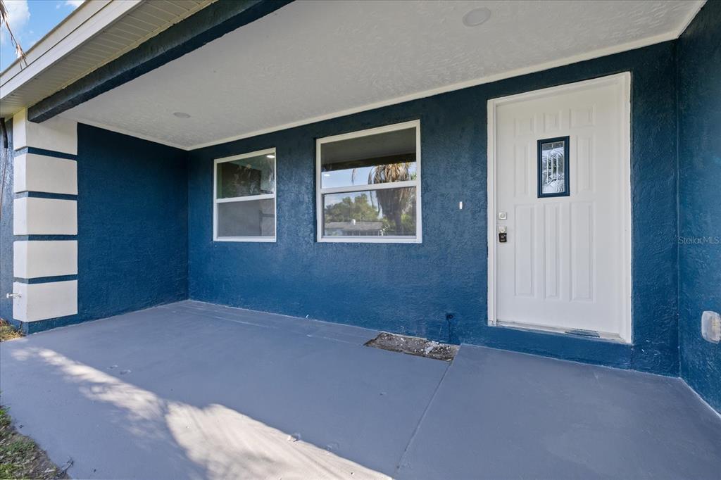 A covered porch with blue stucco walls, a white front door, and gray concrete flooring — 2698 46TH AVENUE N, ST PETERSBURG, FL