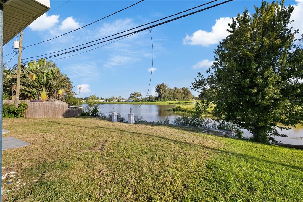 A grassy backyard overlooks a lake with a large tree and a wooden fence — 2698 46TH AVENUE N, ST PETERSBURG, FL