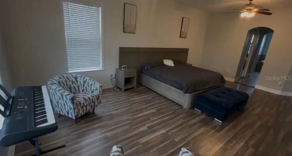 A bedroom features wood-look flooring, a bed with a headboard, a patterned armchair, and a keyboard — 24920 SE HIGHWAY 450, UMATILLA, FL