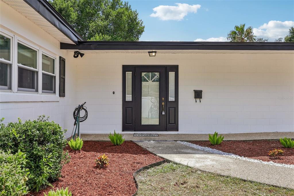The exterior of a white concrete block house features a dark front door and walkway — 4001 TIMBER TRL, ORLANDO, FL