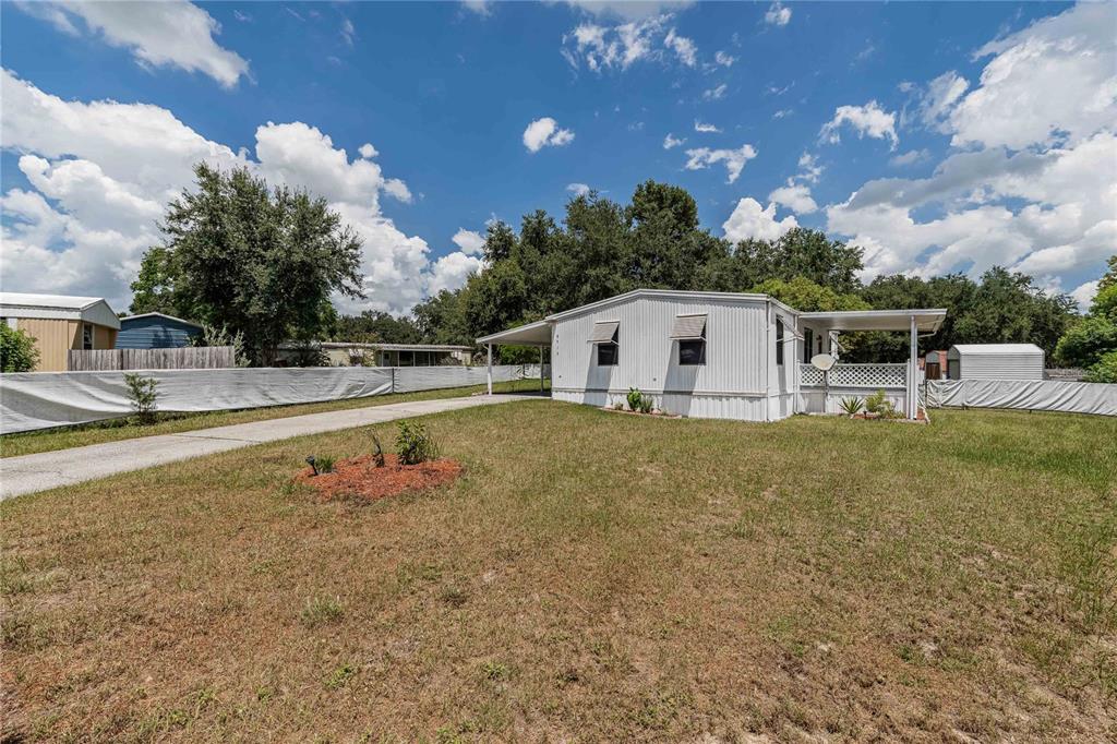 A white mobile home with a carport and a fenced yard under a cloudy sky — 8913 JERICHO COURT, POLK CITY, FL