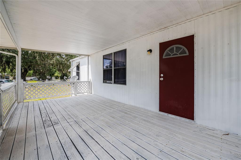 A covered wooden porch features white siding, a red front door, and a lattice railing — 8913 JERICHO COURT, POLK CITY, FL