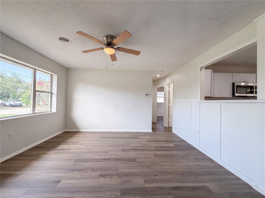 A living room with wood-look flooring, a ceiling fan, and a pass-through to the kitchen — 1516 2ND AVENUE E, BRADENTON, FL