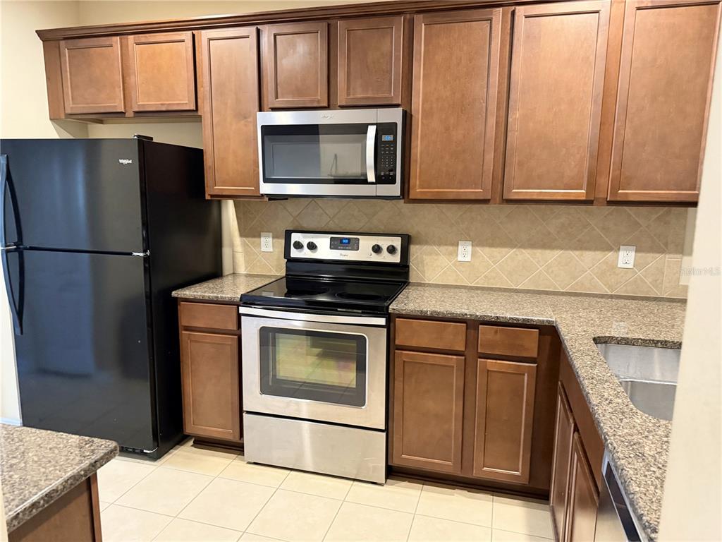 A kitchen features wood cabinets, granite countertops, a black refrigerator, and stainless steel appliances — 15802 STABLE RUN DRIVE, SPRING HILL, FL