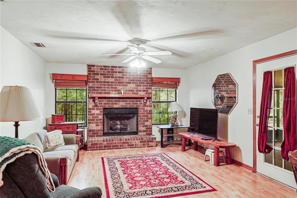 A living room features a brick fireplace, hardwood floors, a ceiling fan, and a red rug — 144 SW ENCHANTED COURT, LAKE CITY, FL