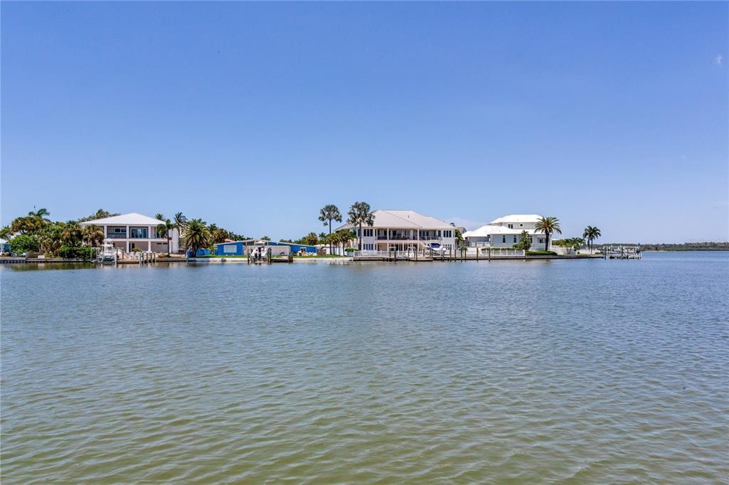 A view of waterfront homes with docks and palm trees along a calm bay — 16458 REDINGTON DRIVE, REDINGTON BEACH, FL