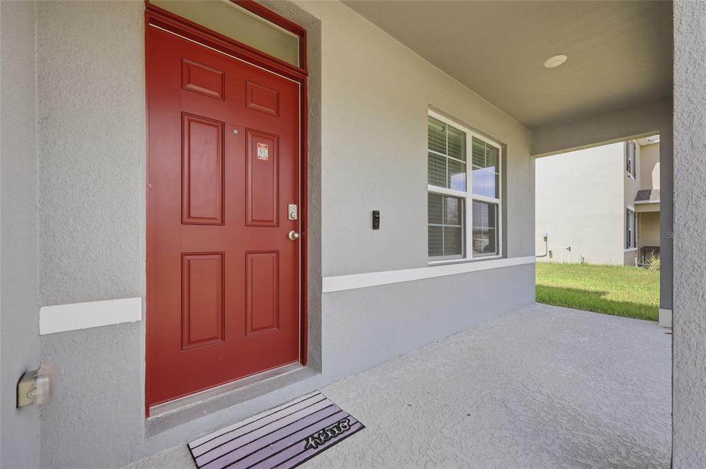 A red front door with a transom window opens onto a covered concrete porch — 583 AUBURN GROVE TERRACE, AUBURNDALE, FL