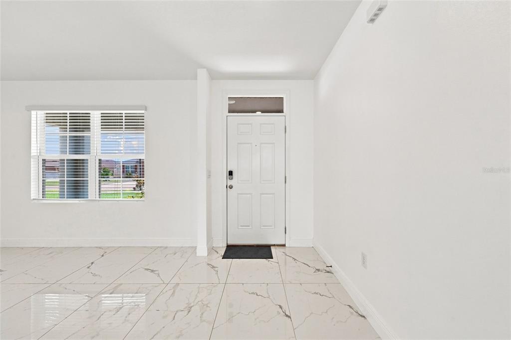 An entryway features white walls, a white front door, and white marble-look tile flooring — 583 AUBURN GROVE TERRACE, AUBURNDALE, FL