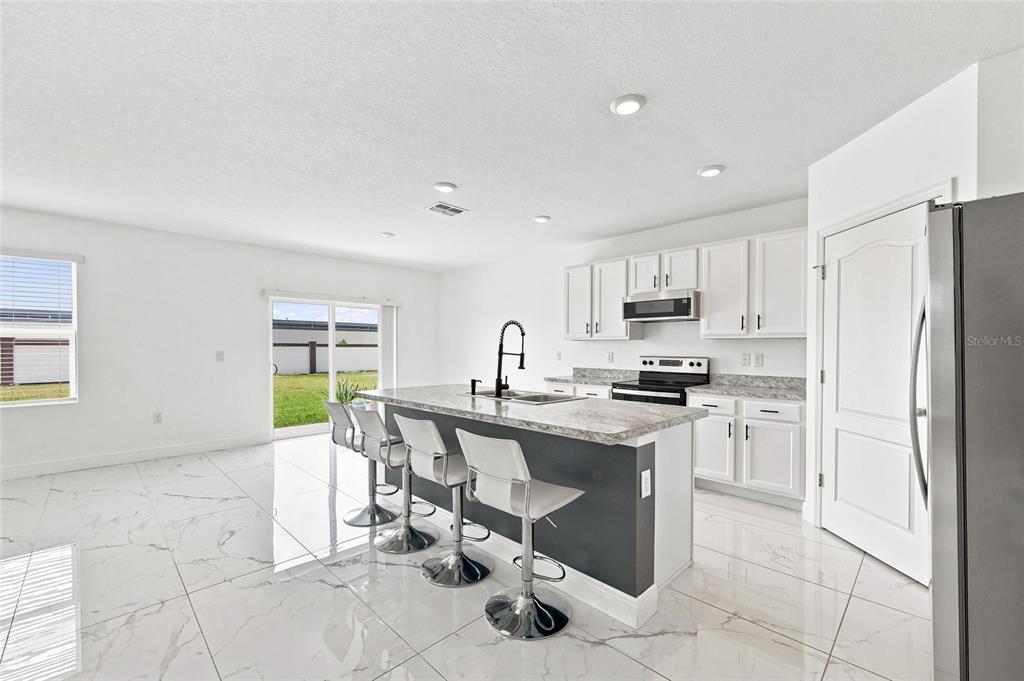 A kitchen features white cabinets, a granite-topped island with bar stools, and white tiled floors — 583 AUBURN GROVE TERRACE, AUBURNDALE, FL