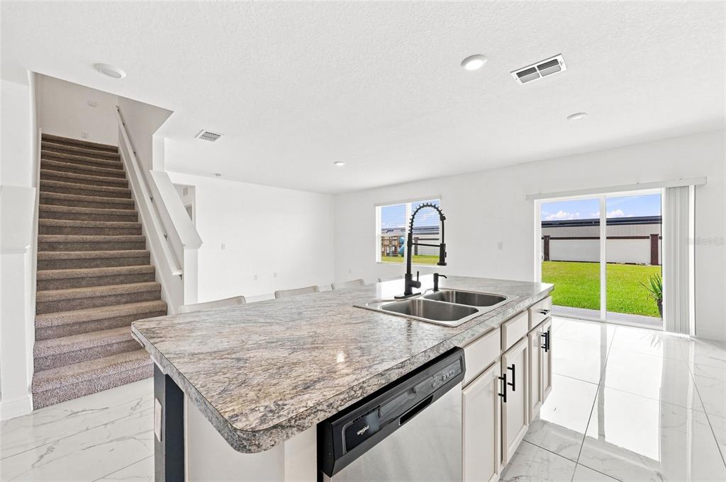 A kitchen island with granite countertops sits before a staircase and sliding glass patio doors — 583 AUBURN GROVE TERRACE, AUBURNDALE, FL
