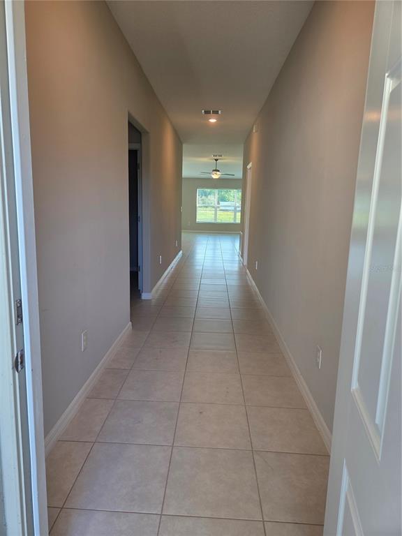 A long hallway with light-colored tile flooring leads toward a room with a ceiling fan — 9306 CHANNING HILL DRIVE, RUSKIN, FL