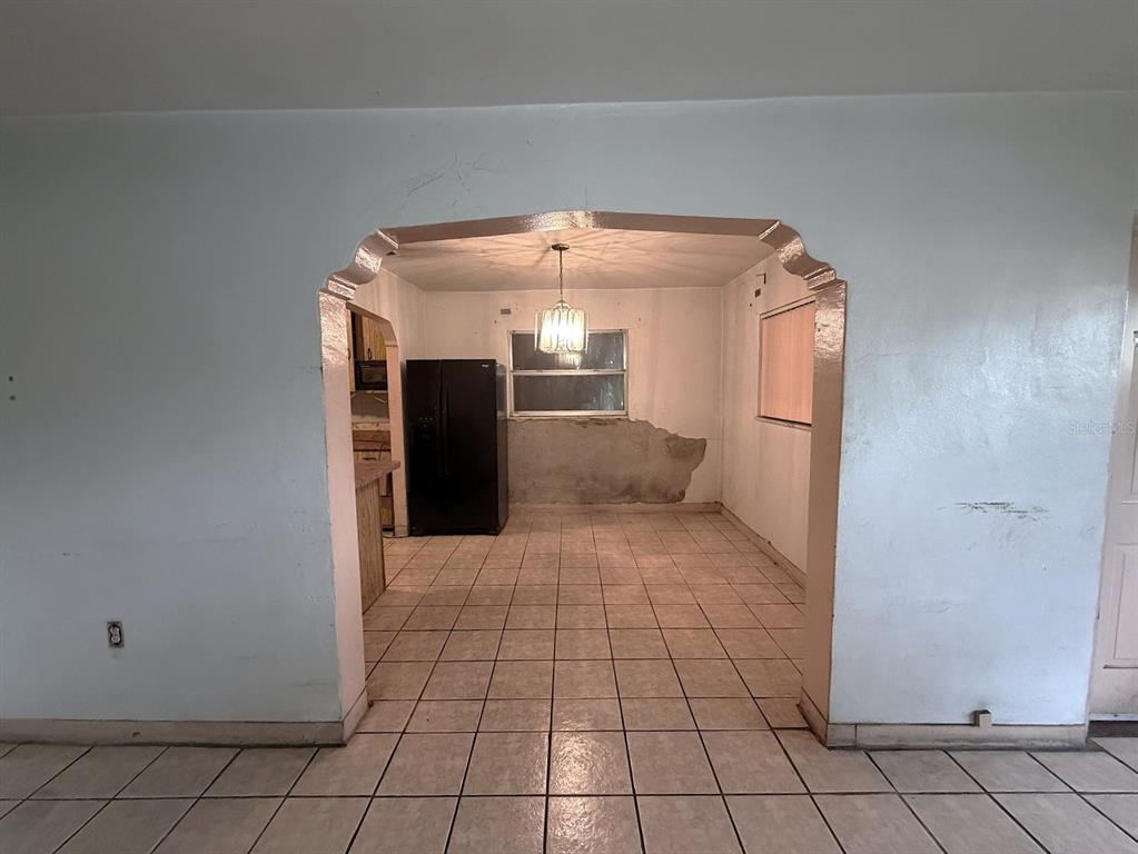 A view through an arched doorway into a kitchen with tiled floors and a refrigerator — 3801 E OSBORNE AVENUE, TAMPA, FL