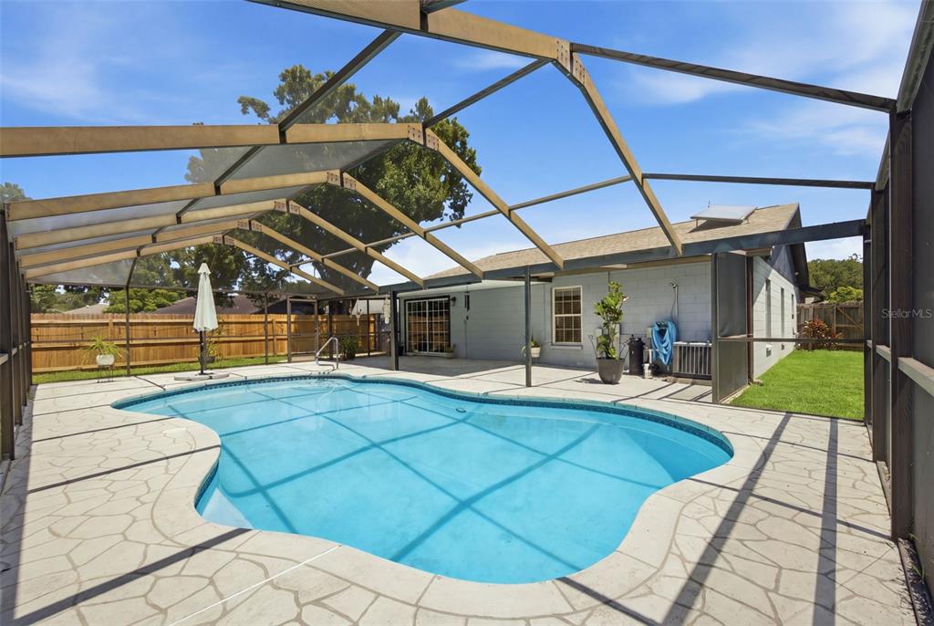 A swimming pool with a screened enclosure sits on a concrete patio behind a house — 1705 CINNABAR COURT, BRANDON, FL